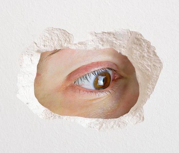 An eye looking through a hole in some drywall to see what is behind it